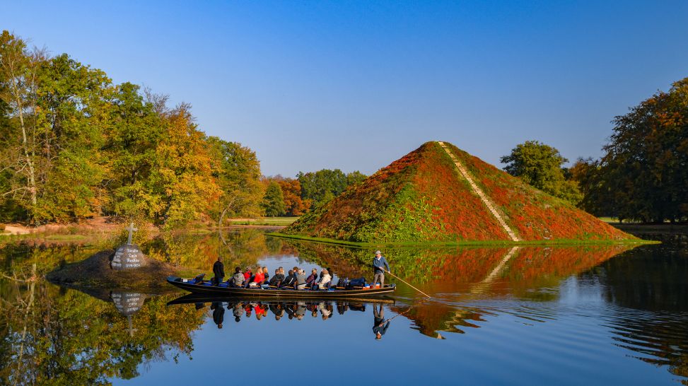 Ein Kahn mit Touristen fährt vor der herbstlich bunten Seepyramide im Fürst-Pückler-Park (Bild: picture alliance/dpa | Patrick Pleul)