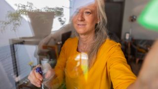 Eine Frau putzt ein Fenster (Quelle: IMAGO/Westend61)