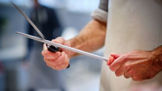 Person schleift ein Messer mit einem Wetzstahl (Quelle: IMAGO / robertkalb photographien)