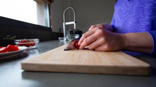 Eine Frau schneidet eine Tomate auf einem hölzernen Schneidebrett (Quelle: IMAGO/CHROMORANGE)
